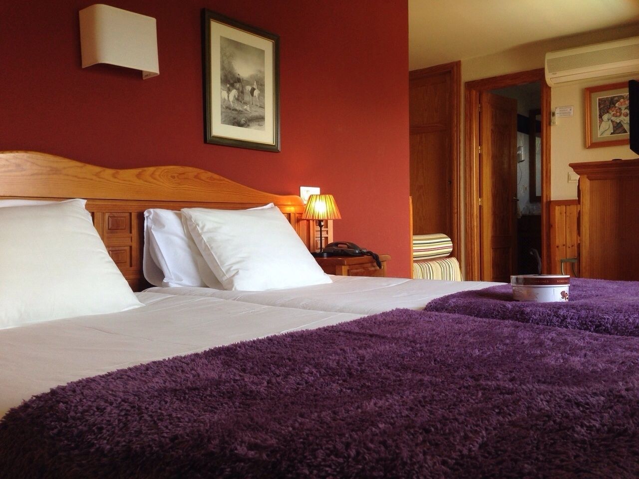 A hotel room with a large bed, a wooden headboard, a bedside lamp, and a framed picture on the wall.