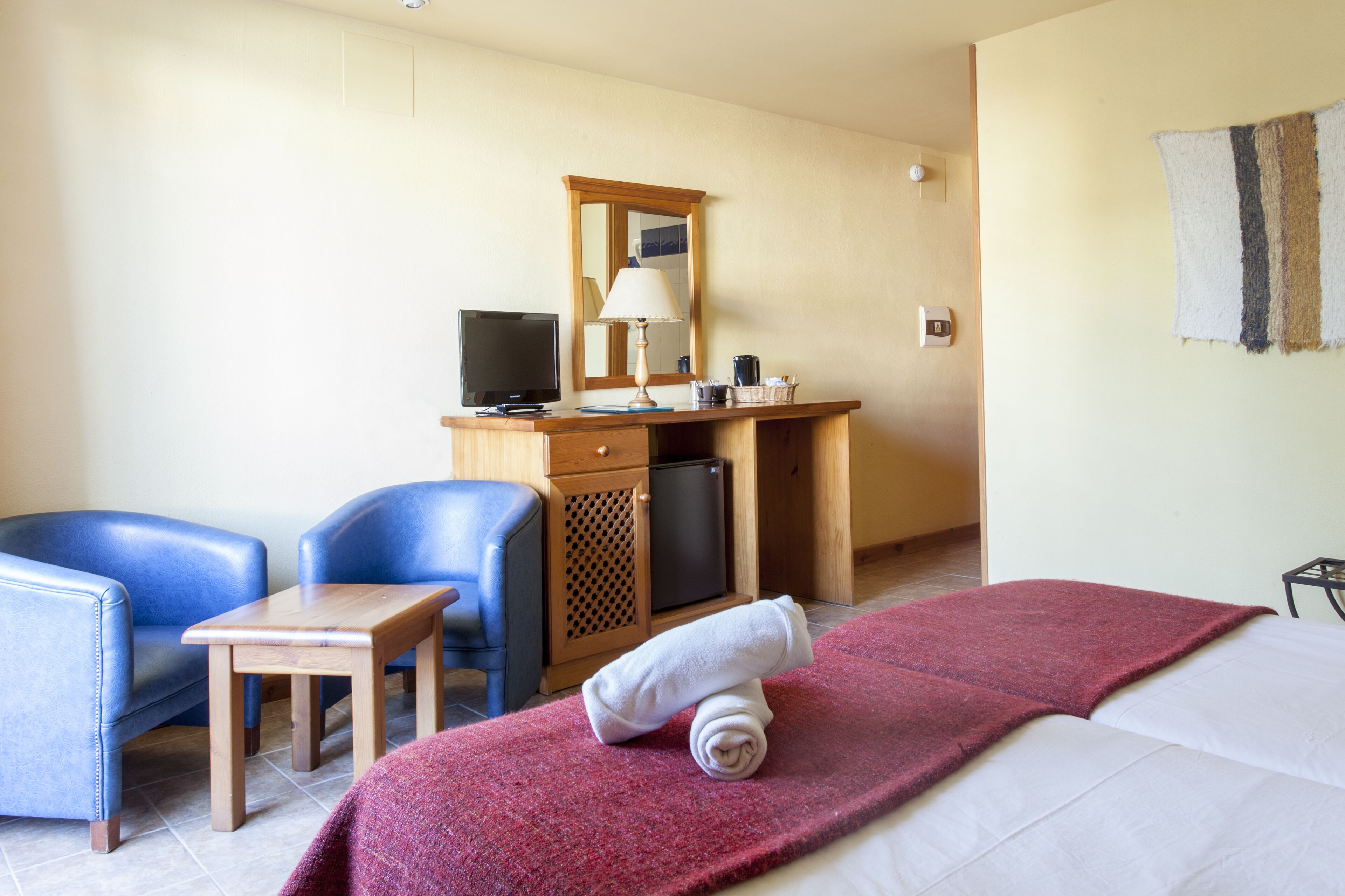 Una habitación de hotel con cama, escritorio con computadora, silla, mesita pequeña y televisor.