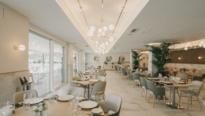 Un comedor amplio con varias mesas dispuestas para comer, una lámpara moderna y grandes ventanales que permiten la entrada de luz natural.