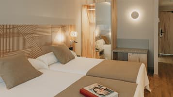 Una habitación de hotel con dos camas, un escritorio y un espejo.
