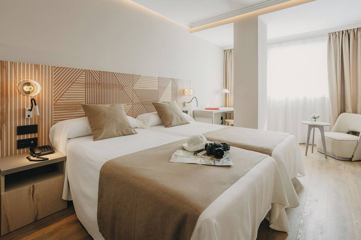 Une chambre d’hôtel avec deux lits, un bureau, une chaise, une lampe et un téléphone sur la table de chevet.