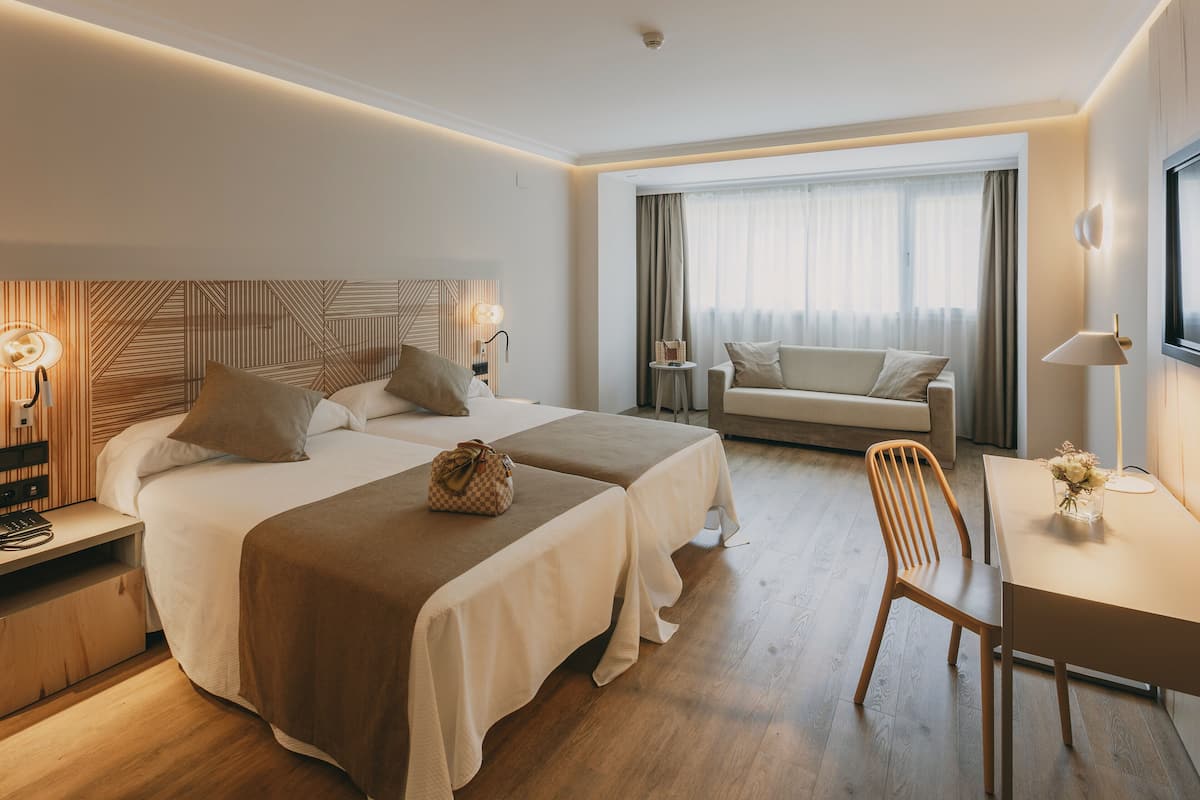 Une chambre d’hôtel avec deux lits, un bureau, une chaise, une télévision et une fenêtre avec des rideaux.