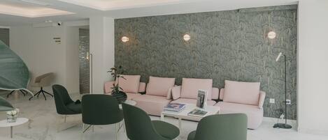 Una sala de estar moderna con un sofá rosa, sillas verdes, una mesita de centro y un papel tapiz estampado.
