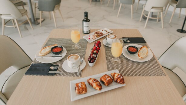A dining table with a bottle of wine, a plate of croissants, and a variety of beverages and condiments. - Hotel El Mirador (Loja)