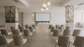 Un salón de conferencias con una larga mesa, sillas, una pantalla de proyector y un espejo grande.