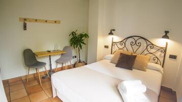 Une chambre à coucher avec un lit, deux lampes de chevet, un bureau avec une chaise et une plante en pot.