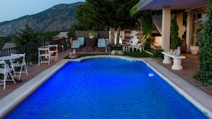 Piscina con borde de piedra, rodeada de muebles de exterior y vistas a montañas.