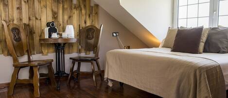 Un dormitorio con cama, pared de madera, una mesa con cafetera y dos sillas.