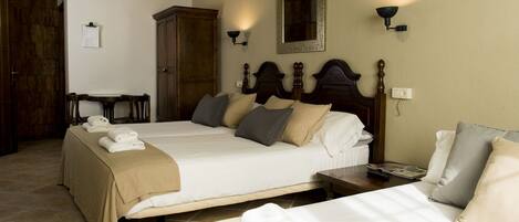 A hotel room with two beds, a wooden wardrobe, a desk, and a mirror.