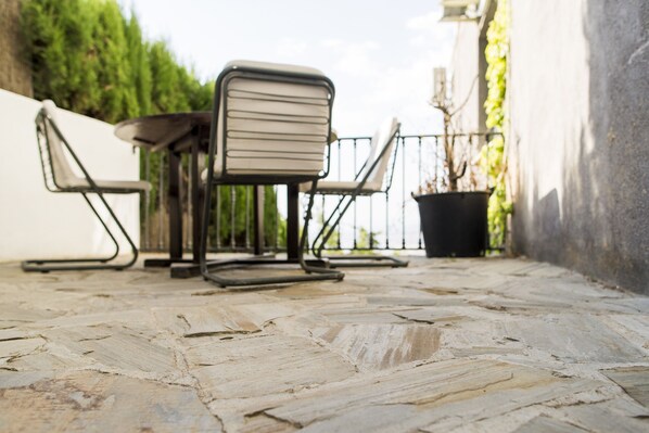 Un patio con una mesa, dos sillas, una planta en maceta y suelo de piedra.