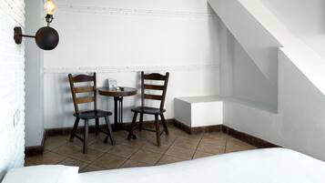 Una habitación pequeña y acogedora con dos sillas de madera, una mesita y una lámpara fijada a la pared.