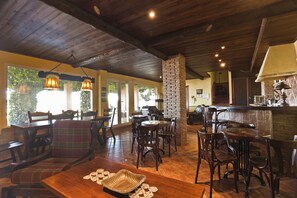 Un restaurante con mesas y sillas de madera, una chimenea de ladrillo y amplios ventanales que dejan entrar la luz natural.