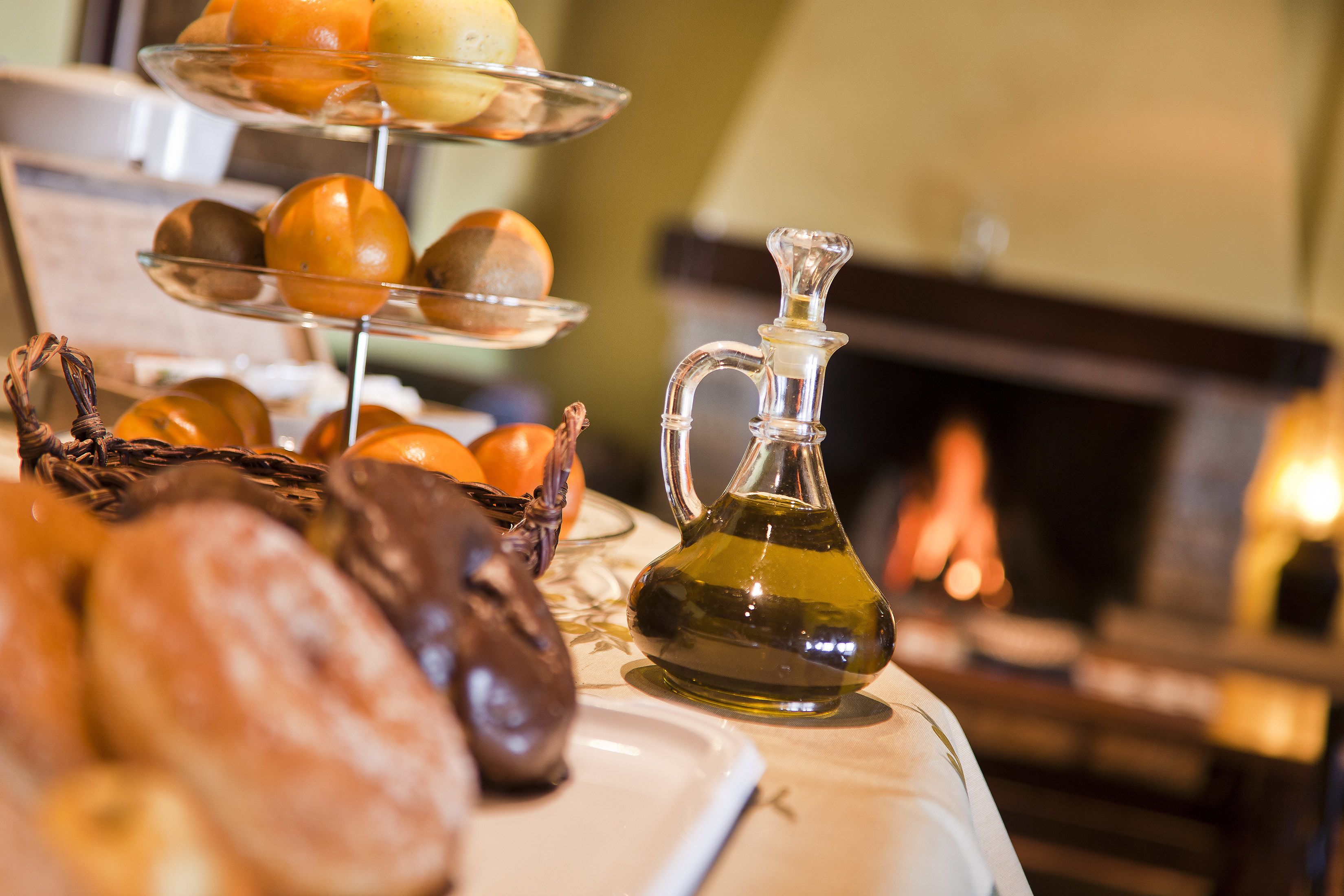 A table with pastries, a glass pitcher of oil, and a fireplace in the background.