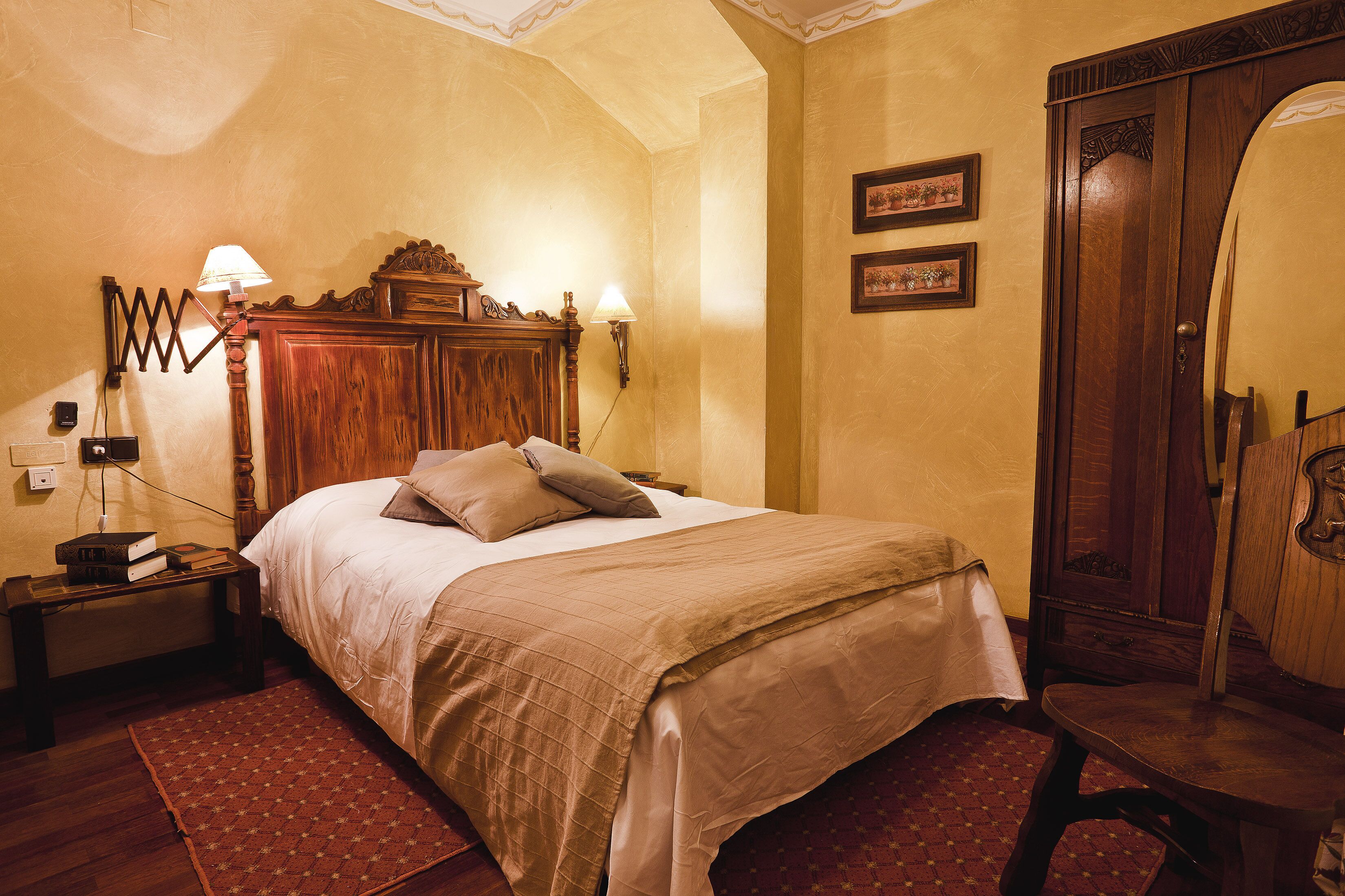 A bedroom with a wooden bed, two bedside lamps, a nightstand, a wooden wardrobe, and a red patterned rug.