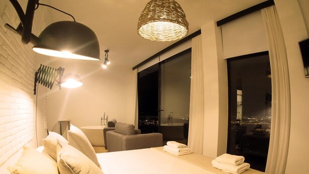Una habitación de hotel moderna con una cama grande, un área de descanso, una bañera y vistas a la ciudad.
