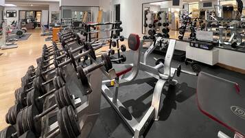 Un gimnasio con varios equipos de levantamiento de pesas, incluyendo mancuernas y discos, y un espejo que refleja los equipos.