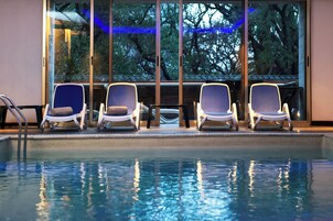 Zona de piscina con cuatro sillas de descanso y barandilla de vidrio.