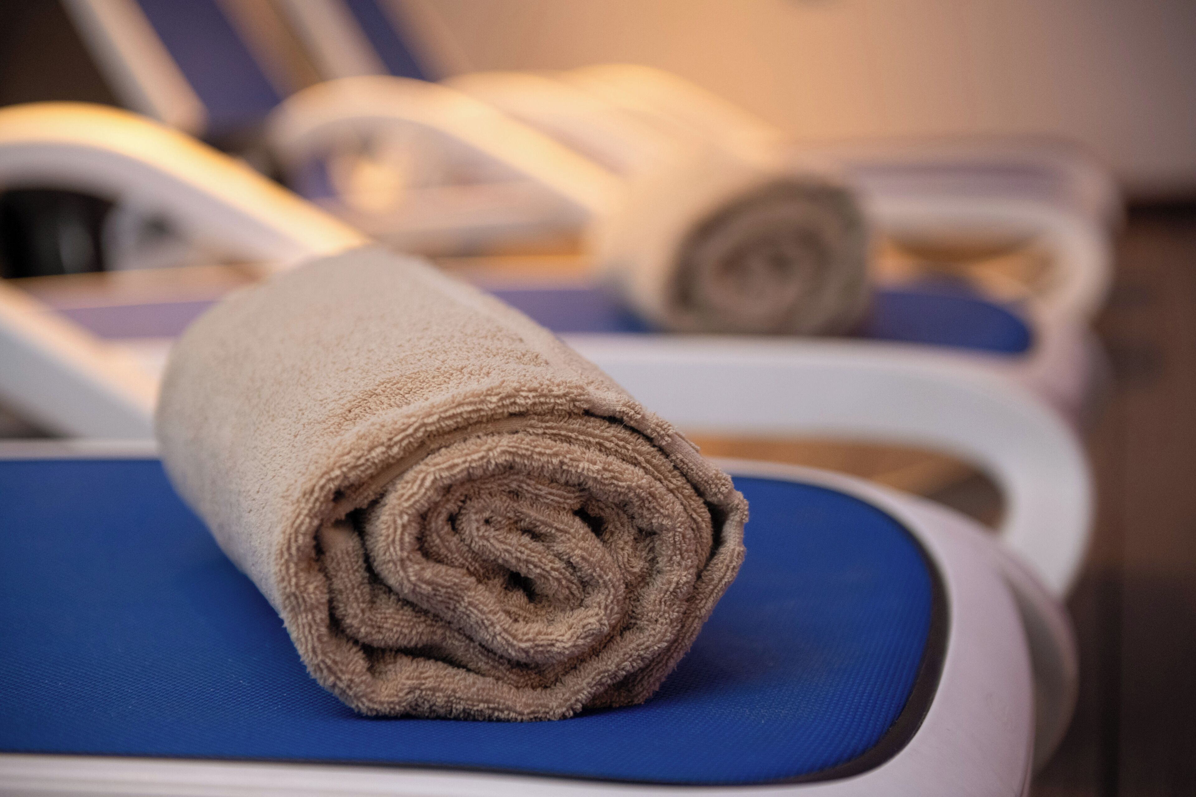 A towel rolled up on a blue chair in a room with white walls and a wooden floor.