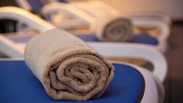 A towel rolled up on a blue chair in a room with white walls and a wooden floor.