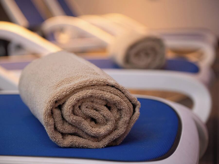 A towel rolled up on a blue chair in a room with white walls and a wooden floor.