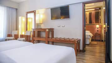 Habitación de hotel con dos camas, un escritorio de madera, una silla, un televisor y un baño visible a través de una puerta abierta.