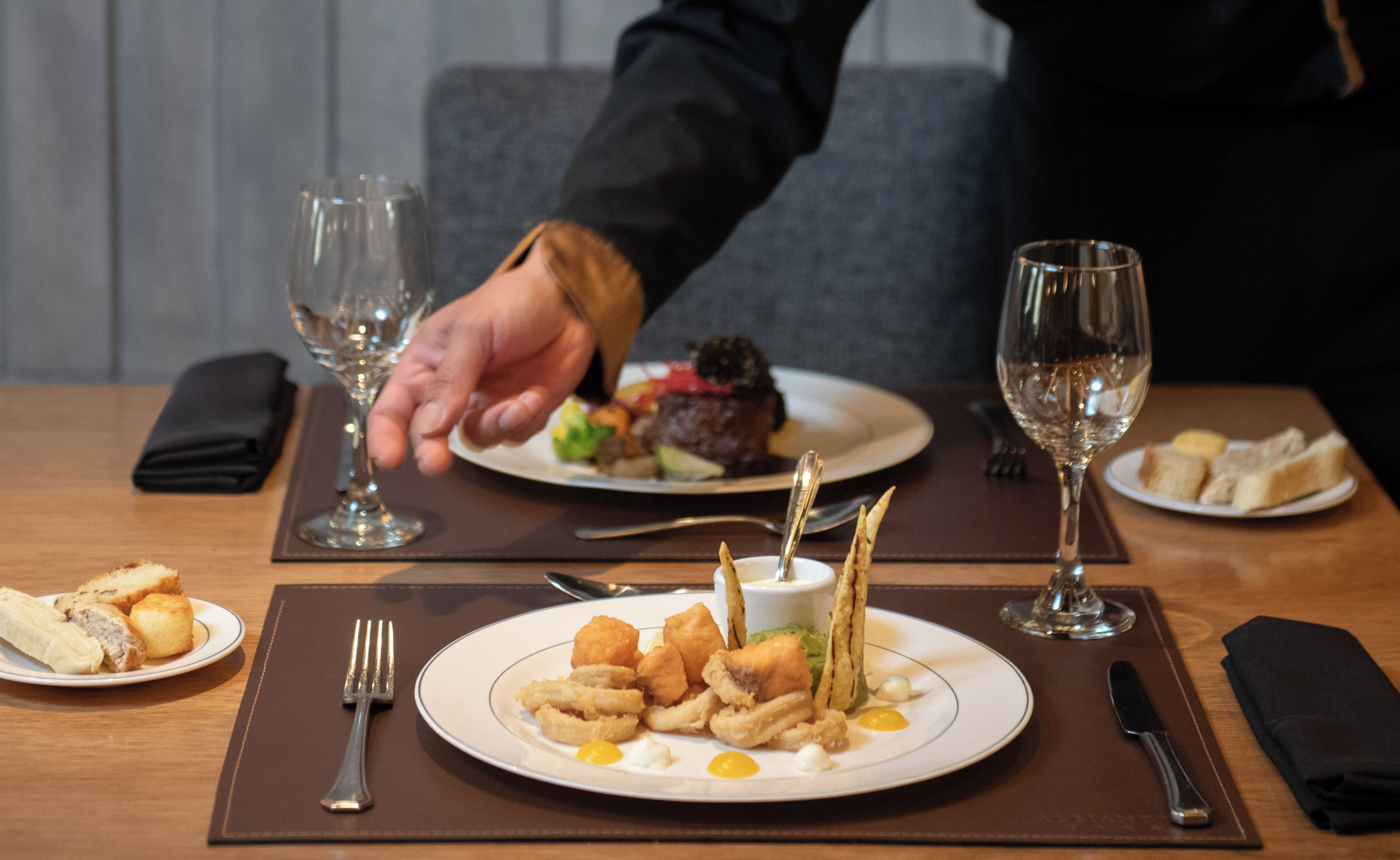 A dining table with plates of food, cutlery, and glasses.