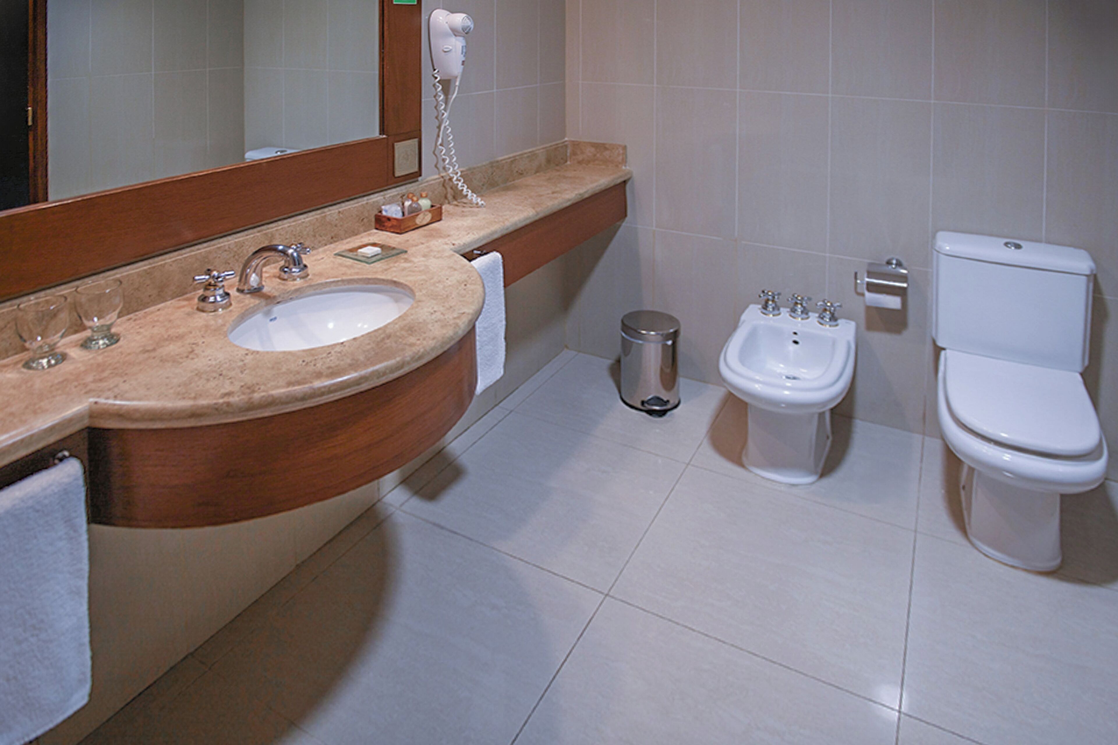 A bathroom with a sink, mirror, vanity, towel, bidet, toilet, and trash can.