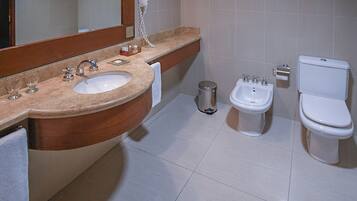 A bathroom with a sink, mirror, vanity, towel, bidet, toilet, and trash can.