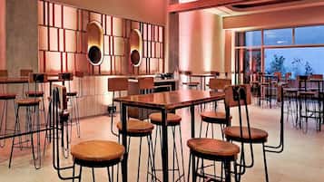 Un comedor amplio con varias mesas y sillas, un área de cocina y ventanas grandes que ofrecen vistas al exterior.