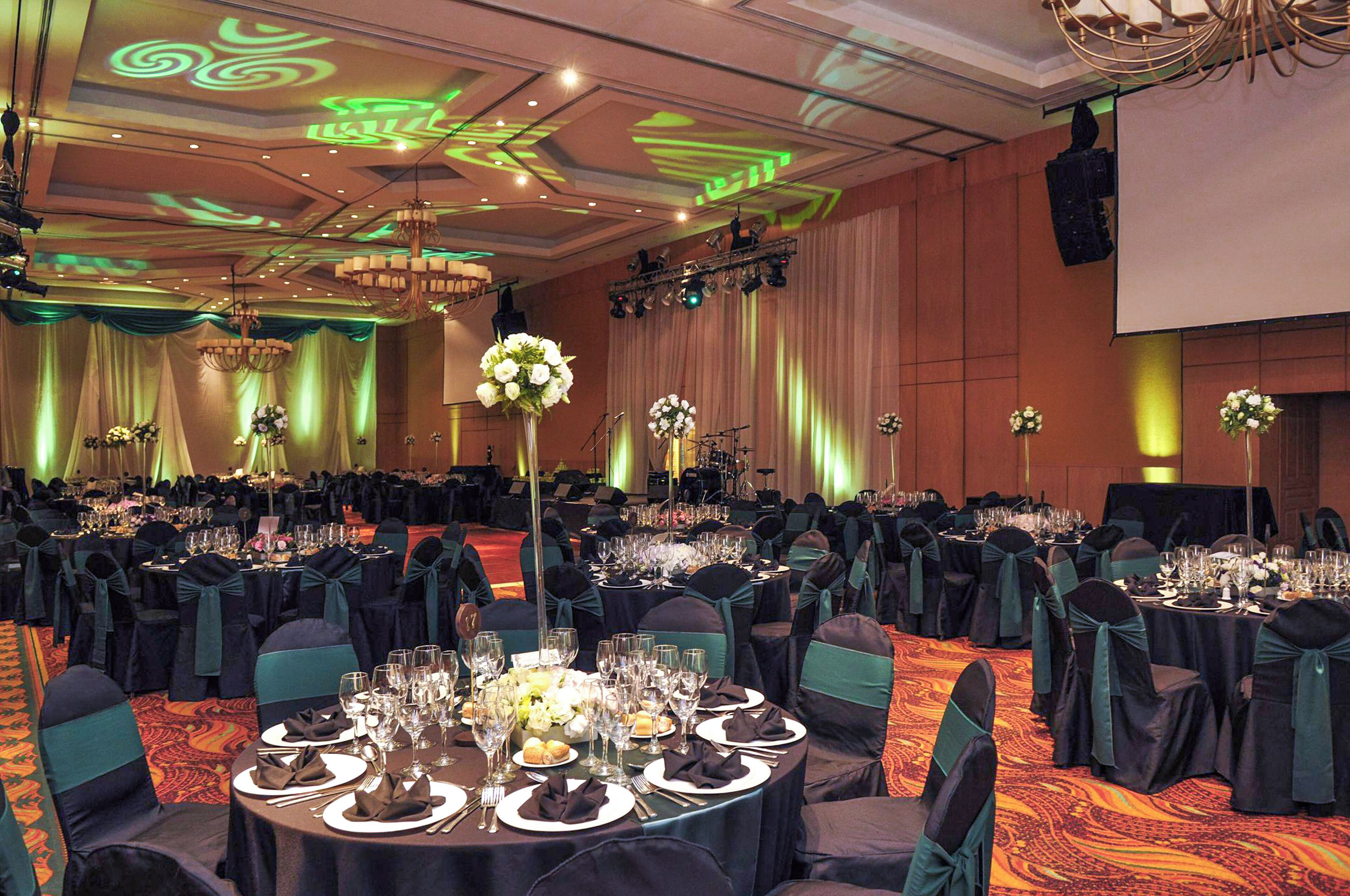 Un salón de banquetes con mesas redondas dispuestas para el servicio, cada una con cubiertos y centros de mesa florales.