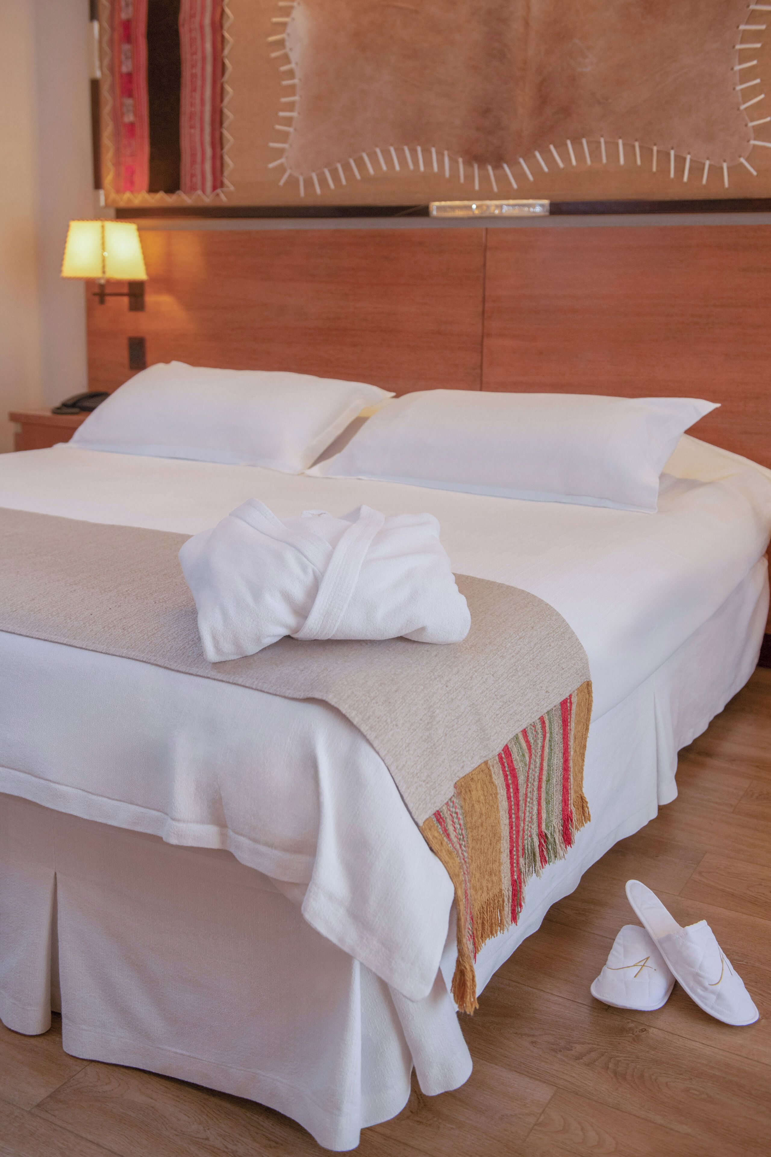 A hotel room with two beds, a wooden headboard, a lamp, and a pair of shoes on the floor.