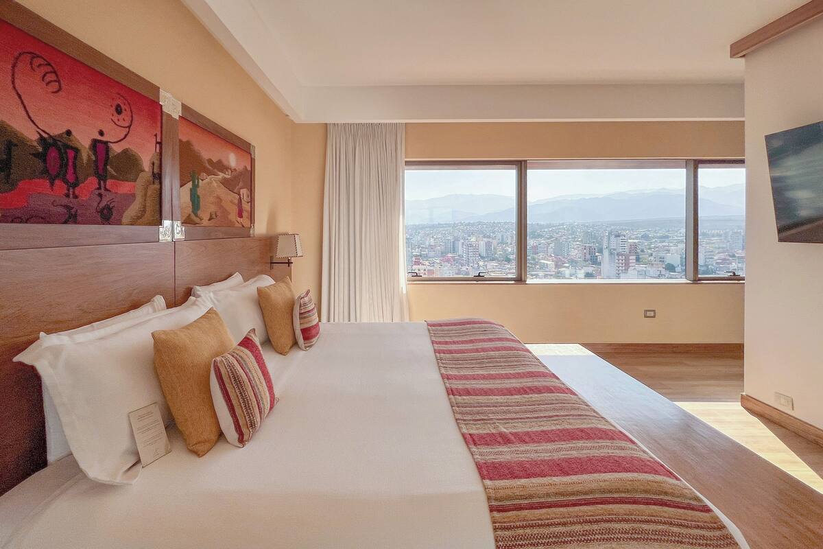 Habitació d'hotel amb un llit gran, vista a la ciutat i un quadre a la paret.