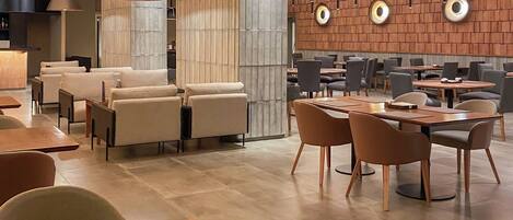Un interior moderno con suelo de madera, una zona de estar central con mesas y sillas, e iluminación colgante.