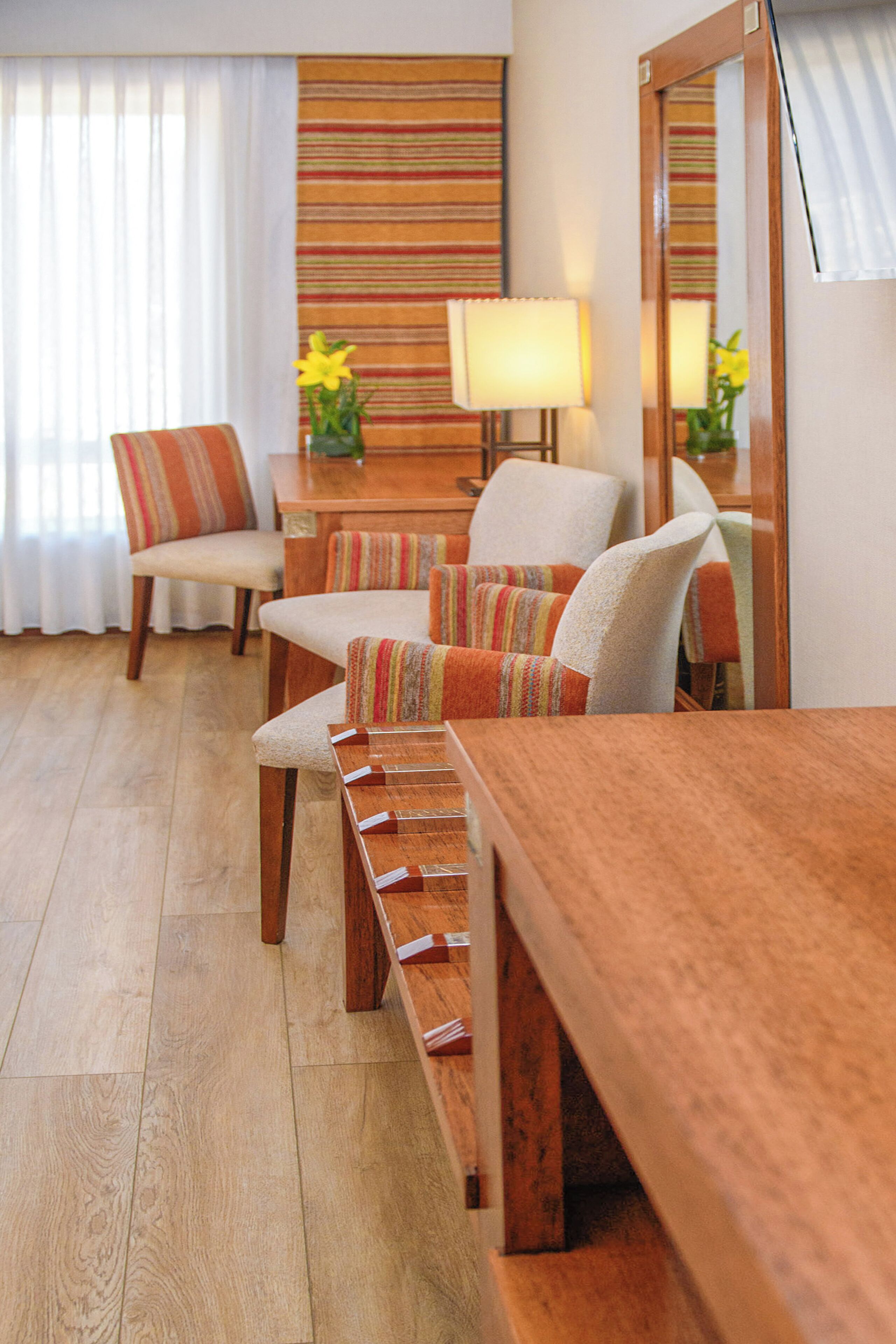 Una mesa de madera para comer con bancos, una pared a rayas y una silla con cojín.
