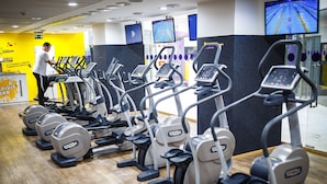 A gym with multiple treadmills and elliptical machines, a man standing near the machines, and a yellow wall with motivational text. - Art Hotel William (Bratislava)