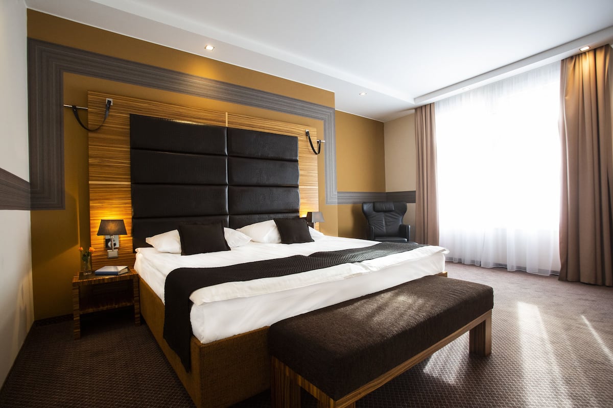 A modern hotel room with a large bed, a bench, a nightstand, and a lamp.