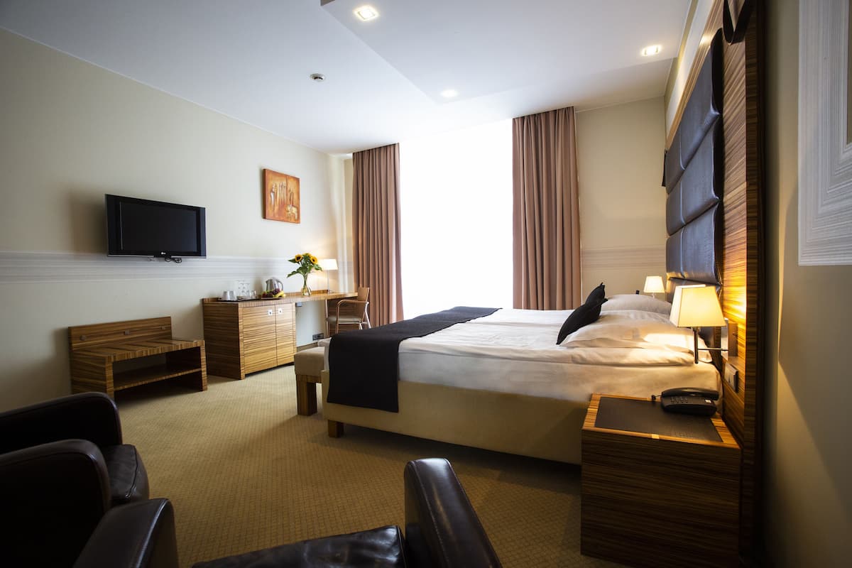 A hotel room with a bed, bedside tables, a TV, a desk, and a chair.
