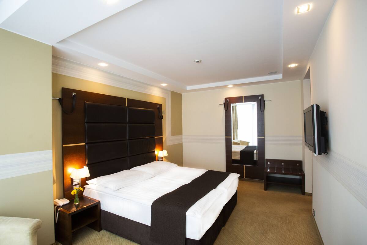 A hotel room with a large bed, bedside lamps, a flat-screen TV, and a small bench.