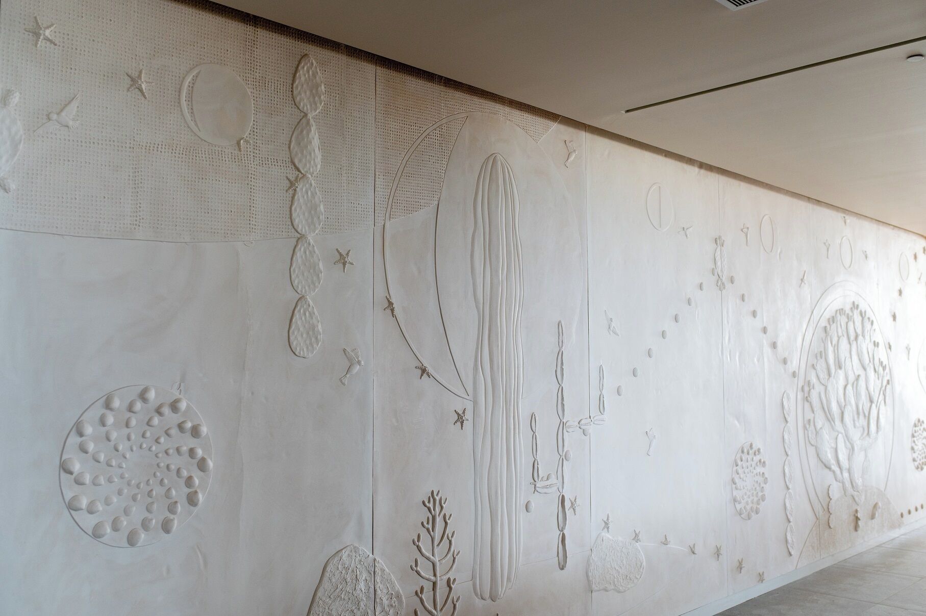 Un mur orné d’un motif texturé et de divers motifs en relief, notamment des étoiles, des oiseaux et des formes abstraites.