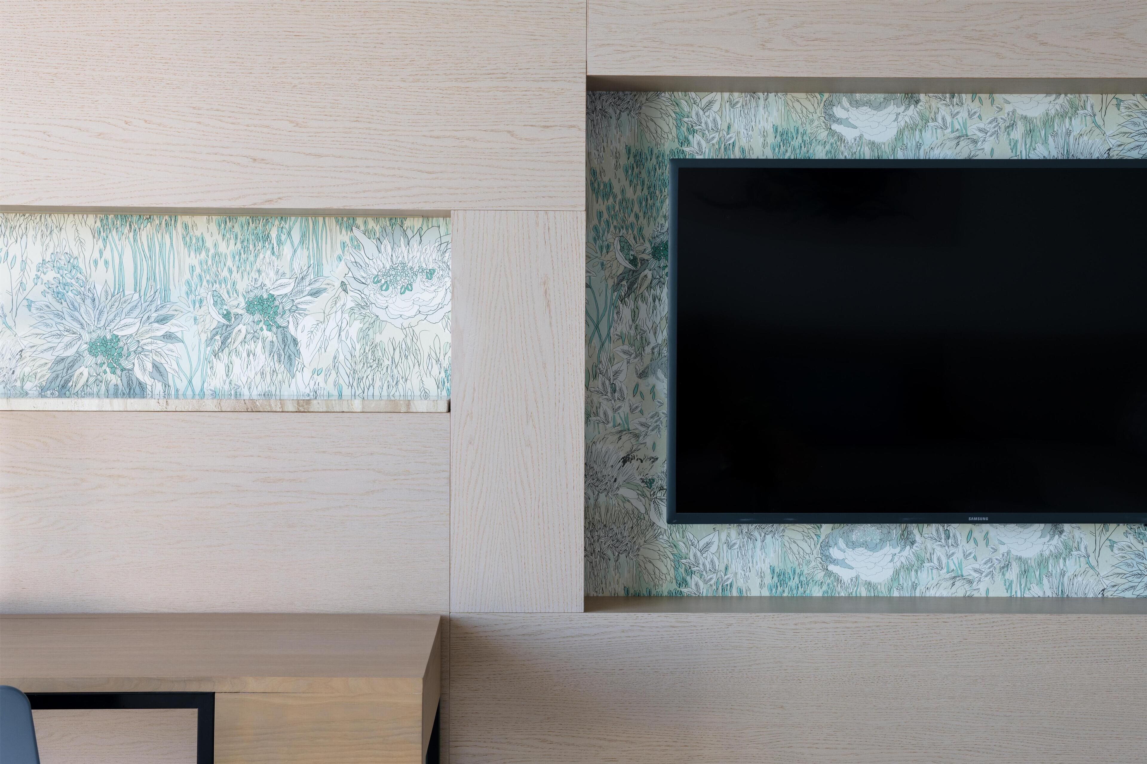 A modern room with a flat-screen TV mounted on a wall with a floral wallpaper design.