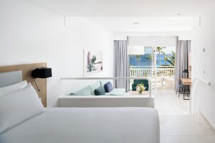 Habitación de hotel con cama, escritorio, silla, balcón con vista al océano y un cuadro en la pared.