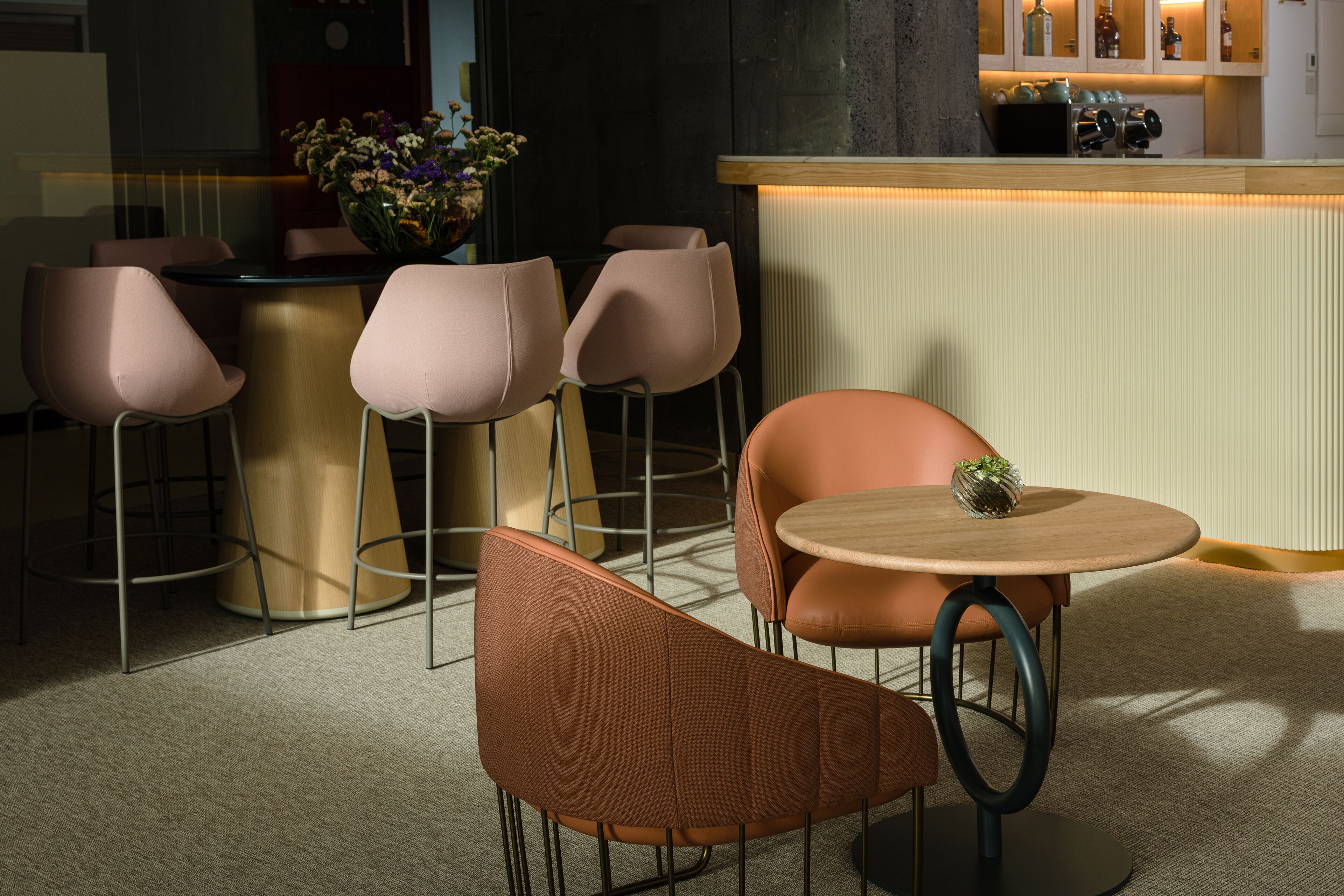 Un comedor moderno con una mesa redonda y cuatro sillas, una zona de bar con mostrador, y un jarrón decorativo con flores.