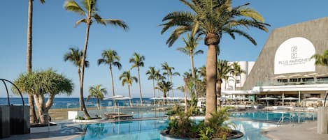 Zona de piscina con palmeras, sillas de descanso y un edificio con un cartel de Plus Fariones Hotels & Apartments.
