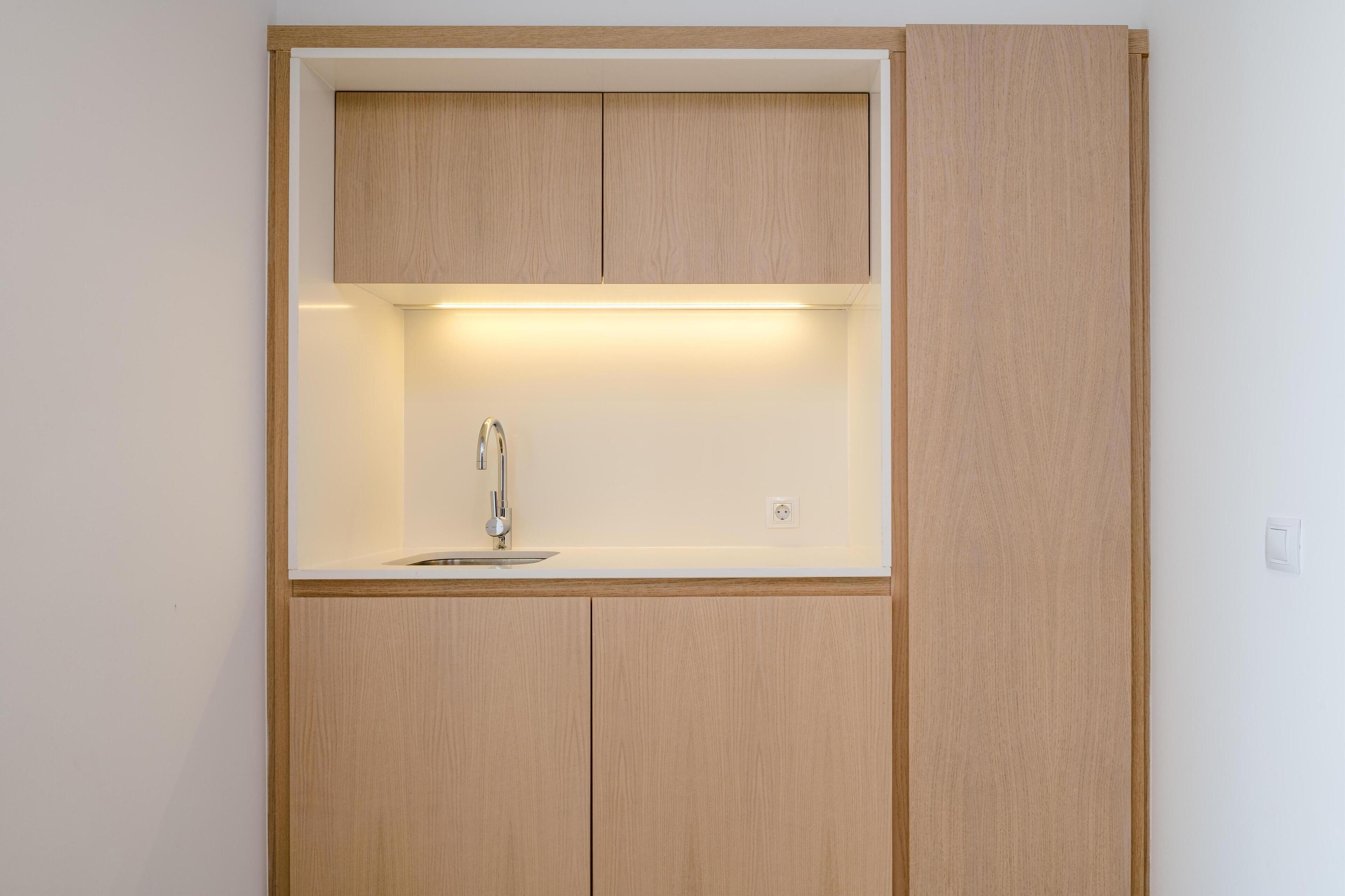 Eine kleine Küche mit integriertem Spülbecken, Holzschränken und Beleuchtung unter den Schränken.