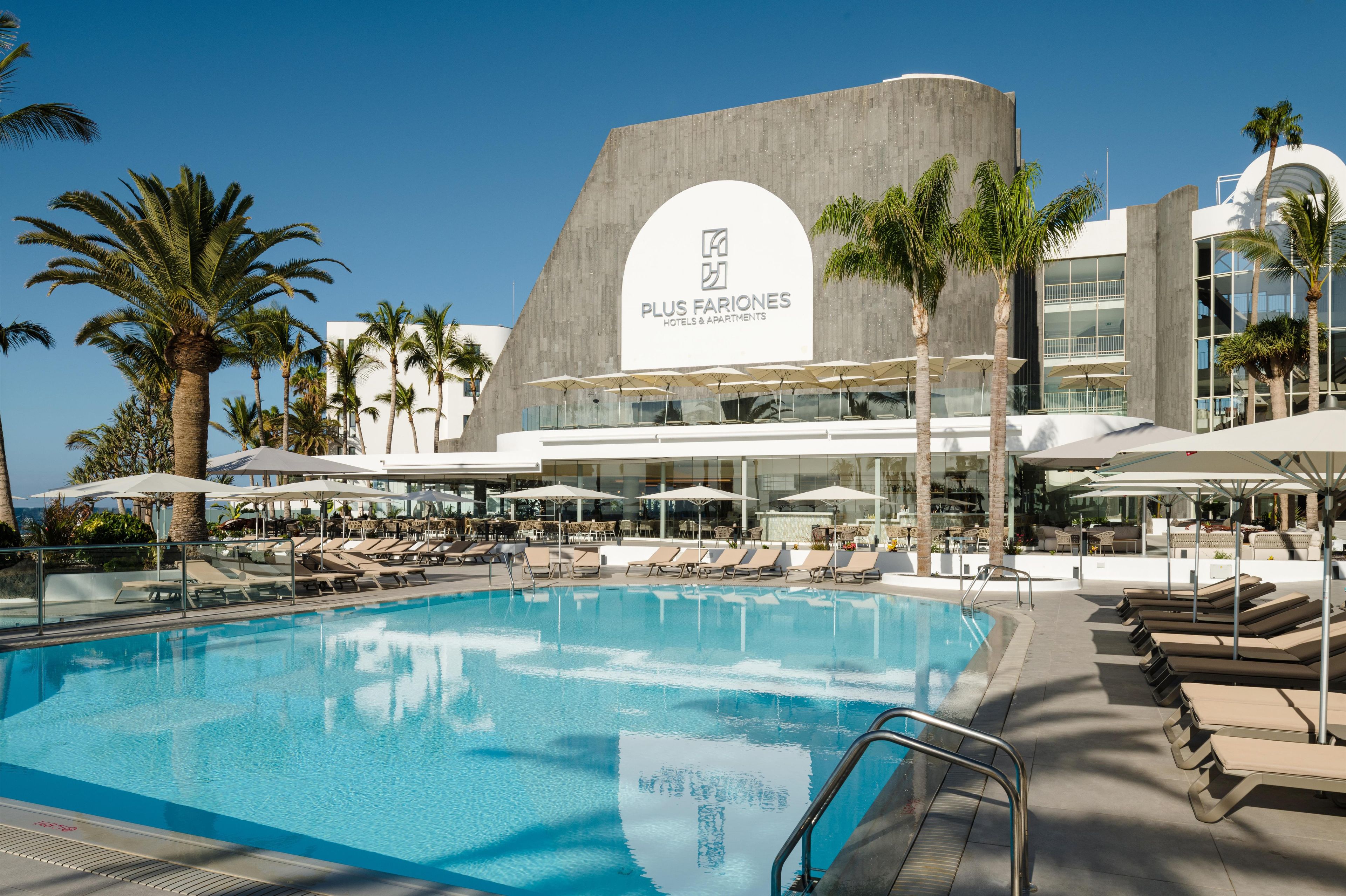 Un hôtel moderne doté d’une grande piscine, de chaises longues et de palmiers.