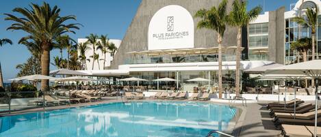 Un hotel moderno con una piscina grande, tumbonas y palmeras.