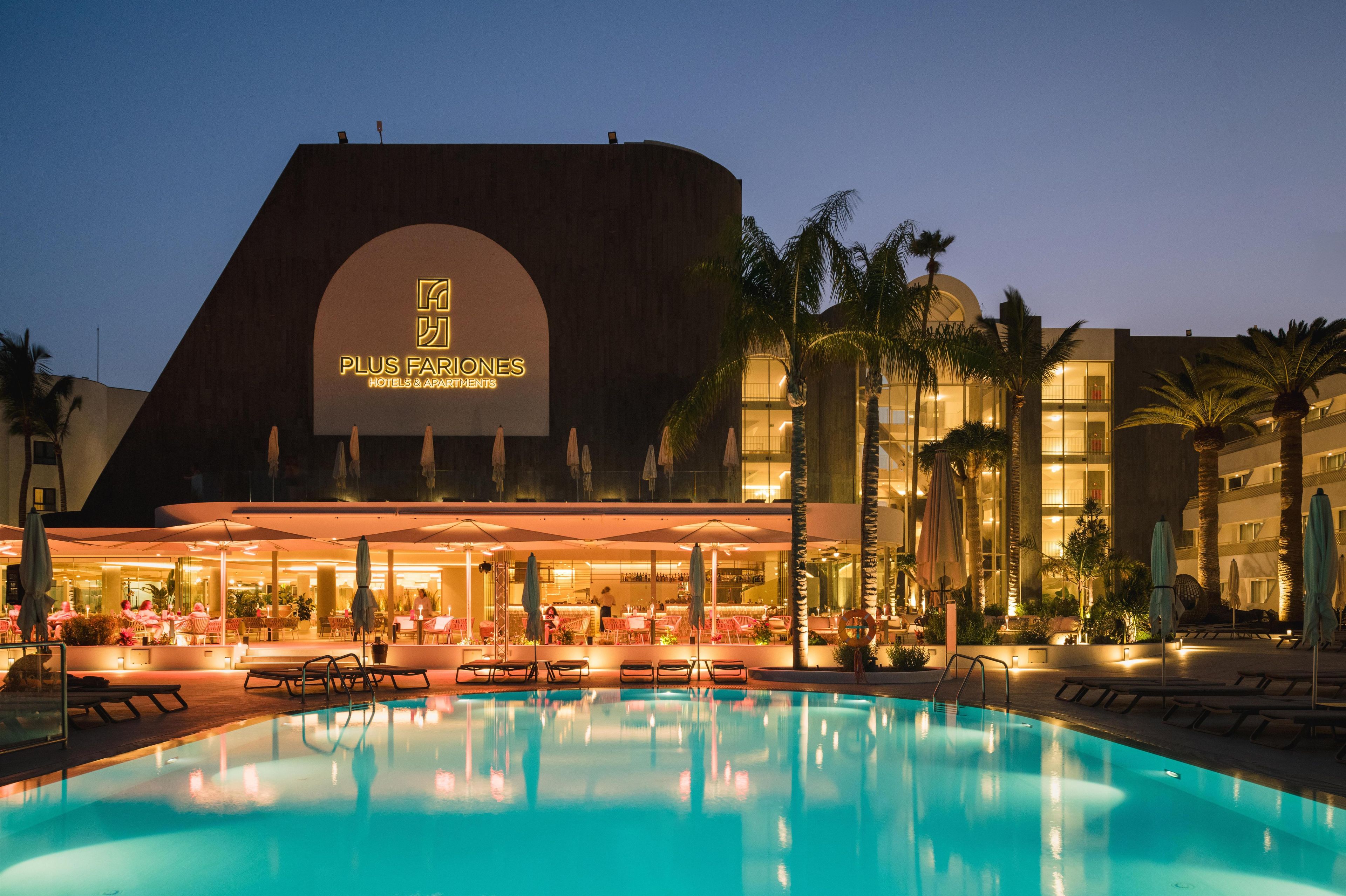 Un hotel con piscina, mobiliario exterior y palmeras.