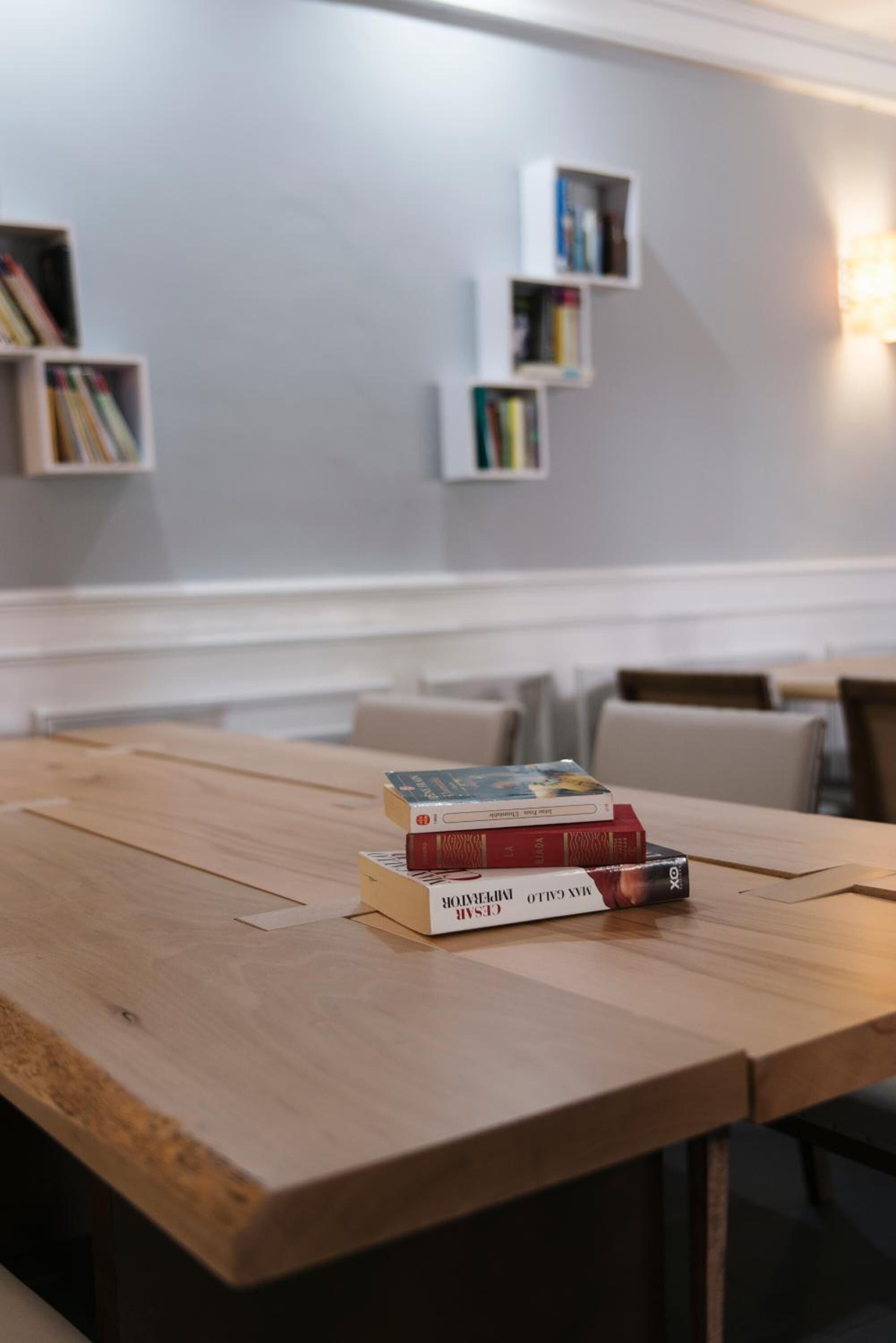 A wooden table with books and a laptop. Shelves with books are mounted on the wall.