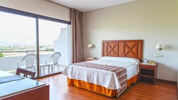 Habitación de hotel con cama, escritorio, sillas, mesita de noche y vistas al exterior.