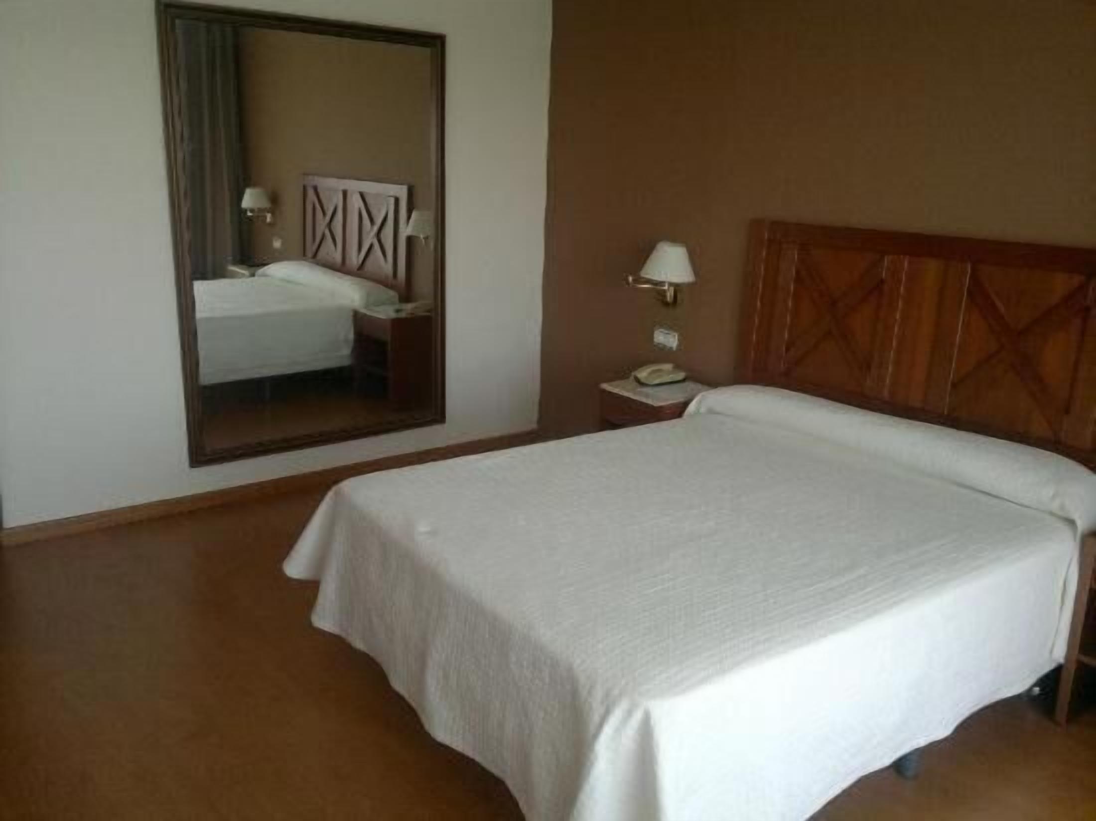 Ein Hotelzimmer mit einem großen Bett, einem Nachttisch mit Lampe und einem Spiegel an der Wand.